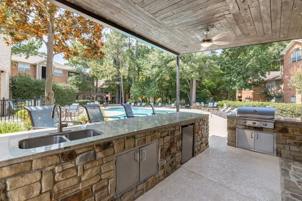 a kitchen with a sink and a grill in front of a pool at Marquis at Kingwood in Kingwood, TX.