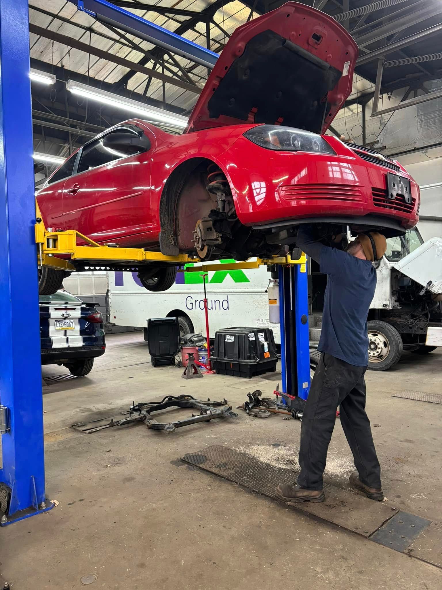 A man is working on a red car on a lift in a garage.