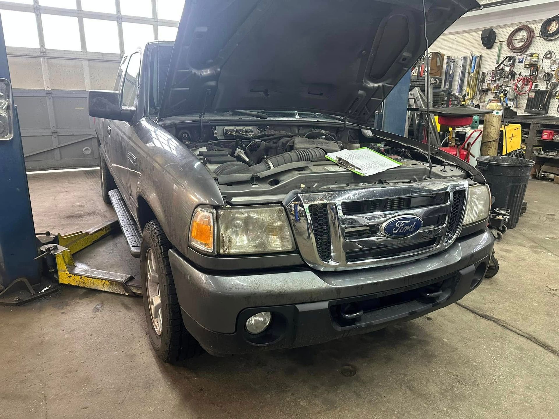 A ford ranger with its hood up is sitting on a lift in a garage.