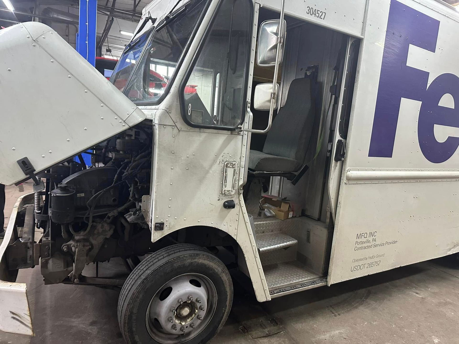 A fedex truck is sitting in a garage with its hood open.