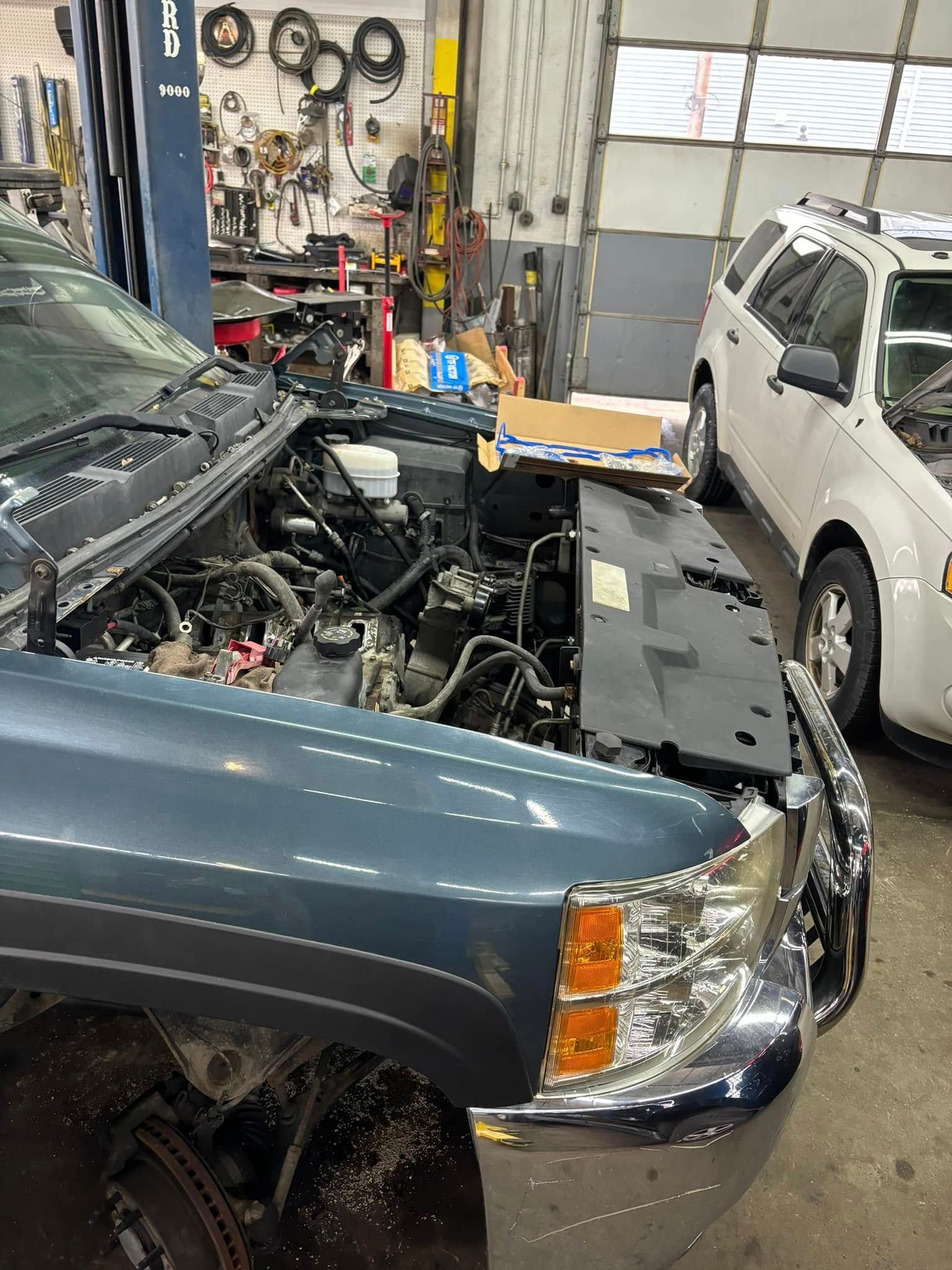 A truck is being worked on in a garage with the hood open.
