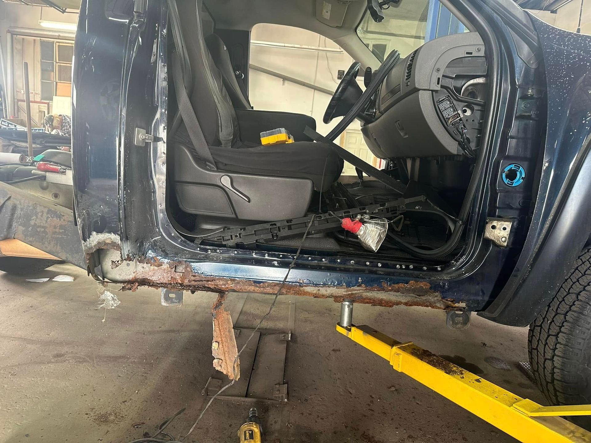 A blue car is sitting on a yellow lift in a garage.