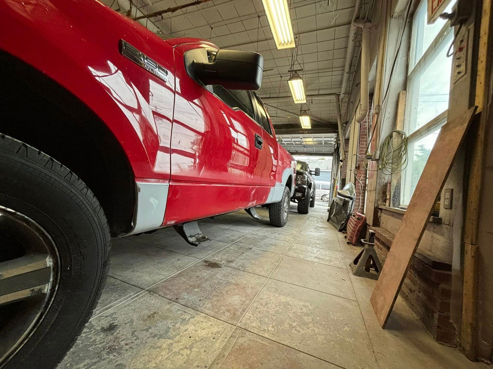 A red truck is parked in a garage next to another red truck.