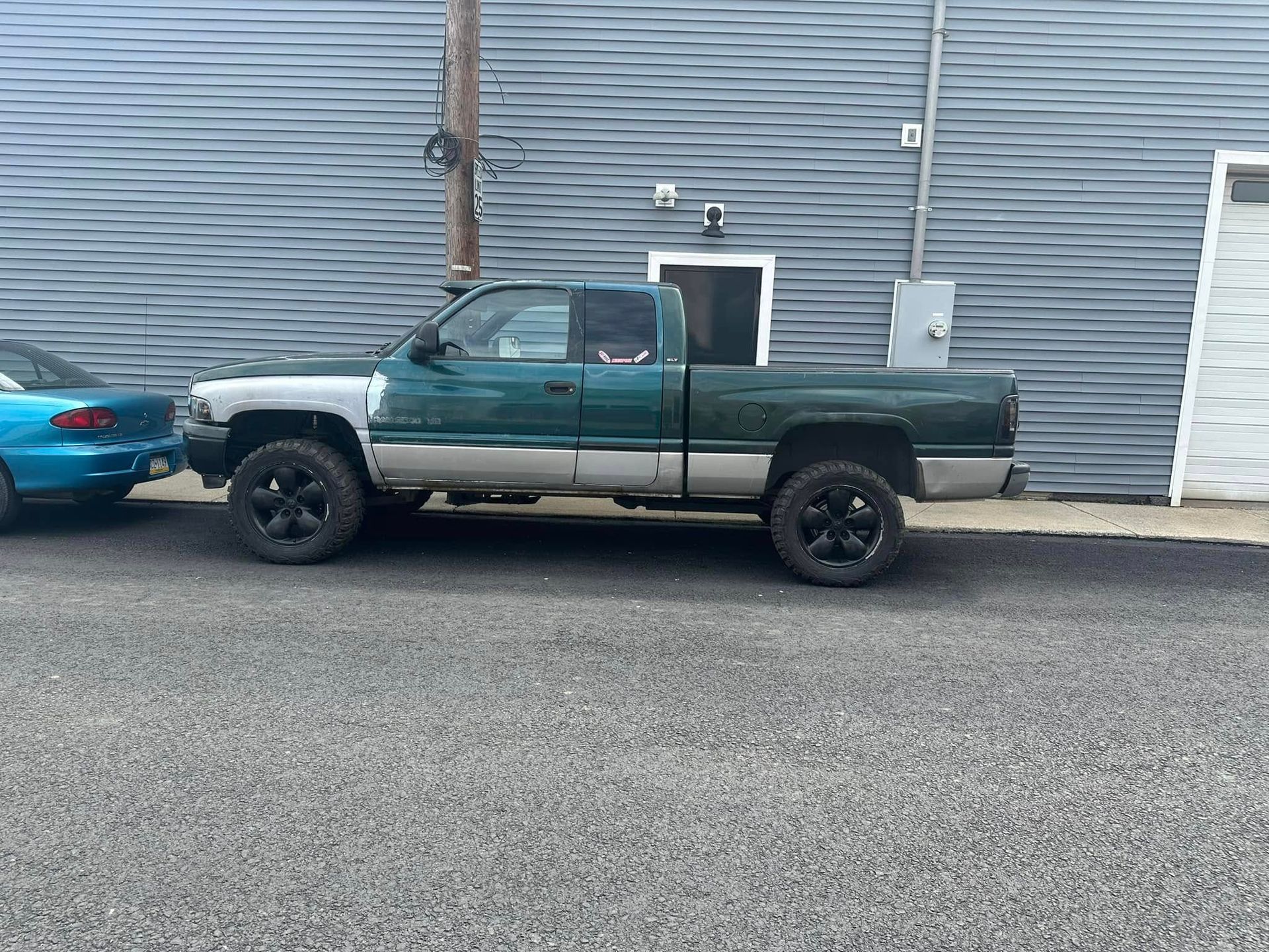 A green truck is parked on the side of the road next to a blue car.