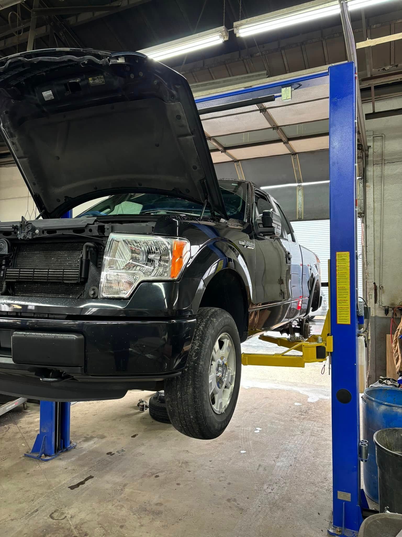 A black truck with the hood up is on a lift in a garage.