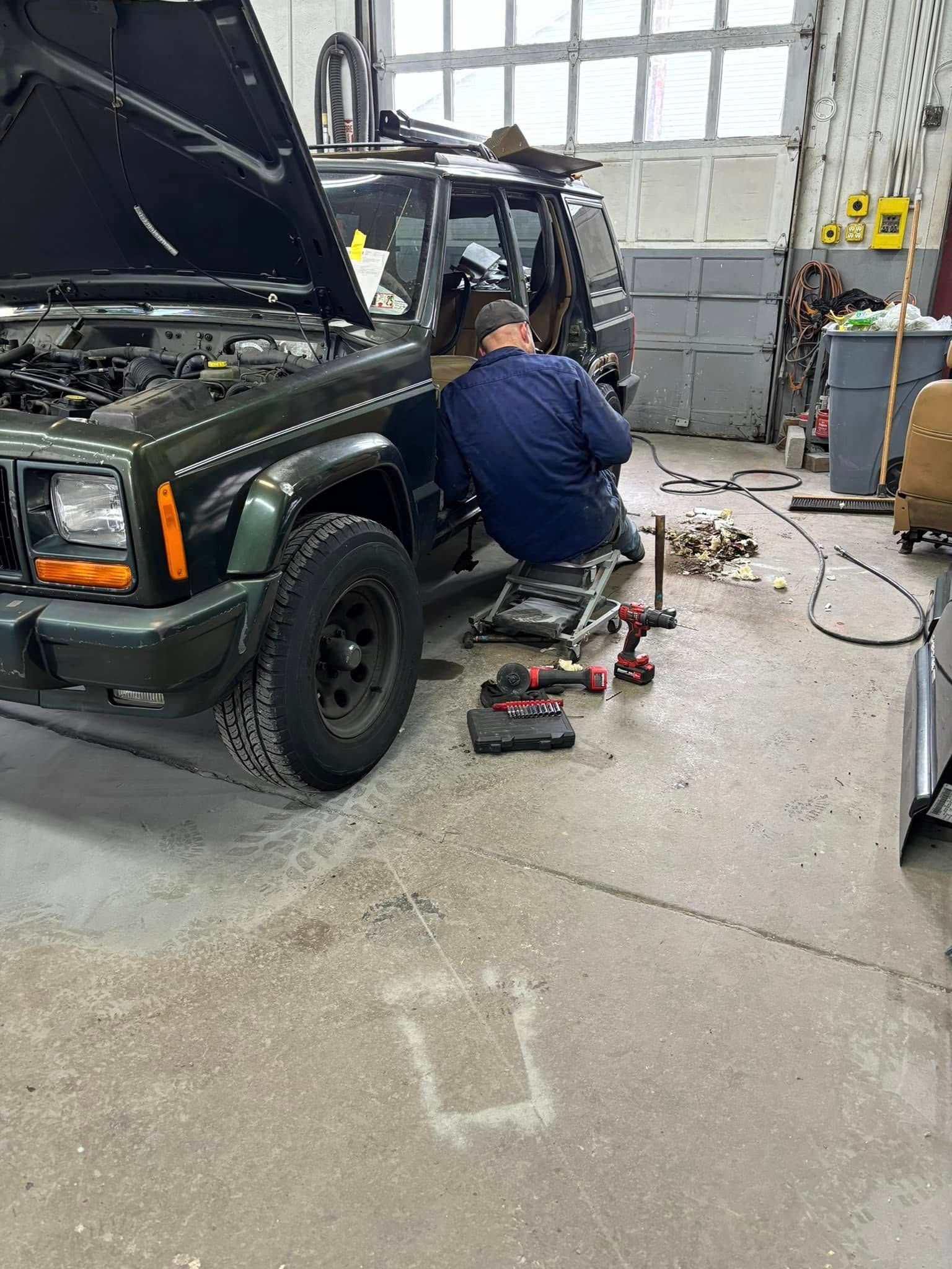 A man is working on a jeep in a garage.