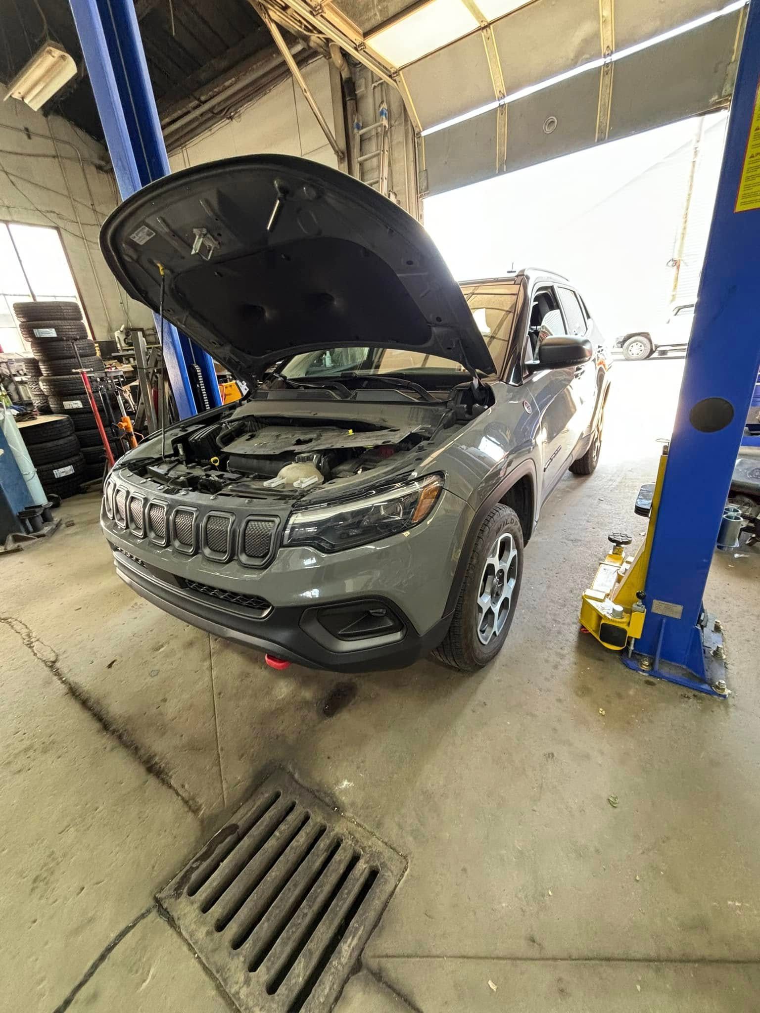A jeep with its hood open is sitting on a lift in a garage.