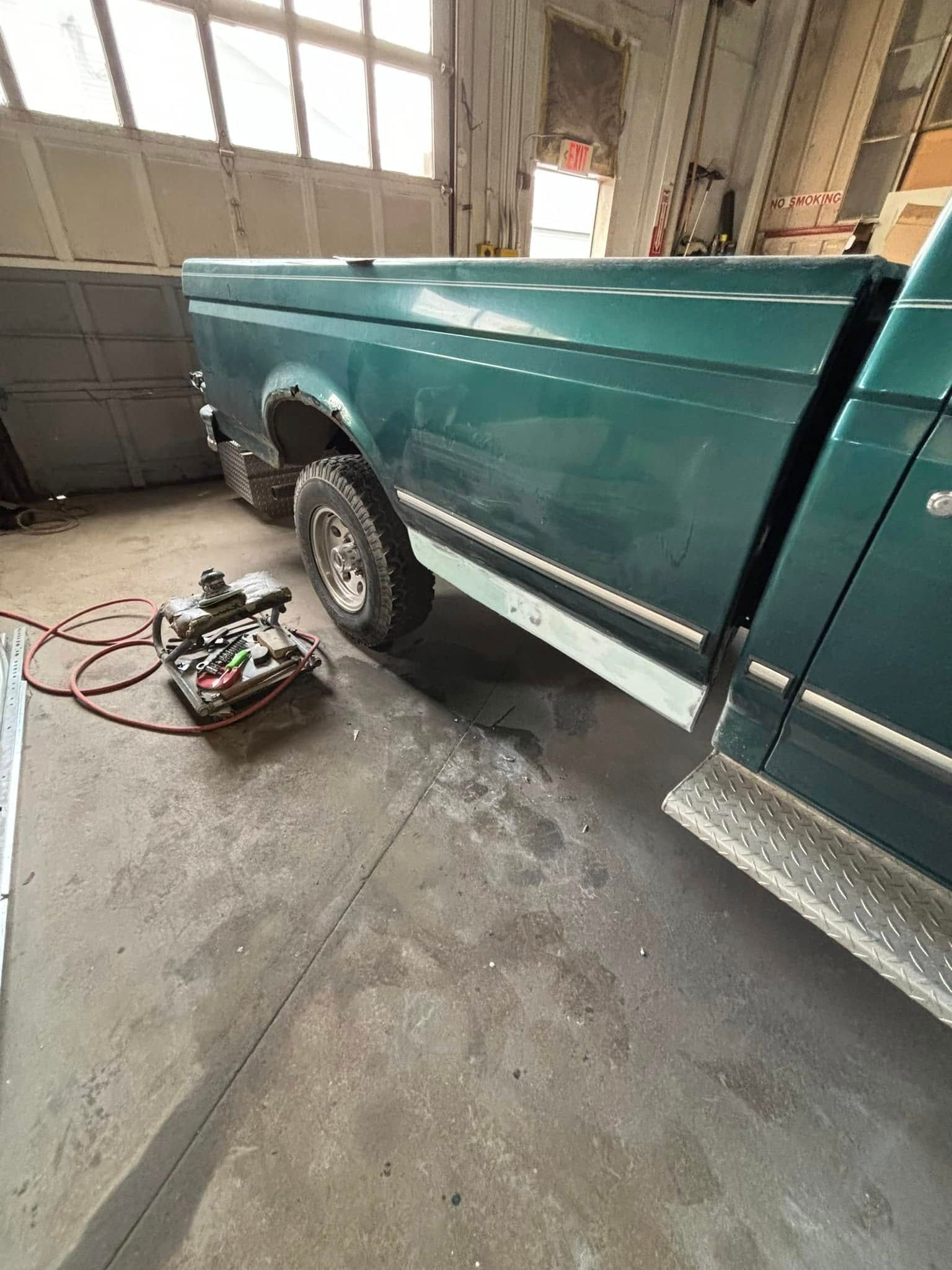 A green truck is parked in a garage next to a garage door.