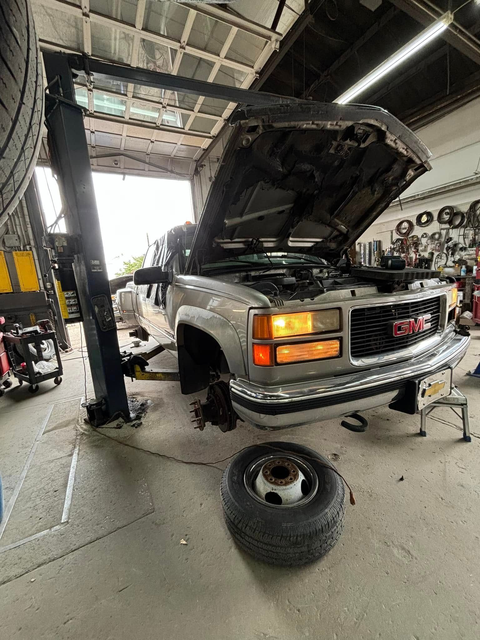 A truck with the hood up is sitting on a lift in a garage.
