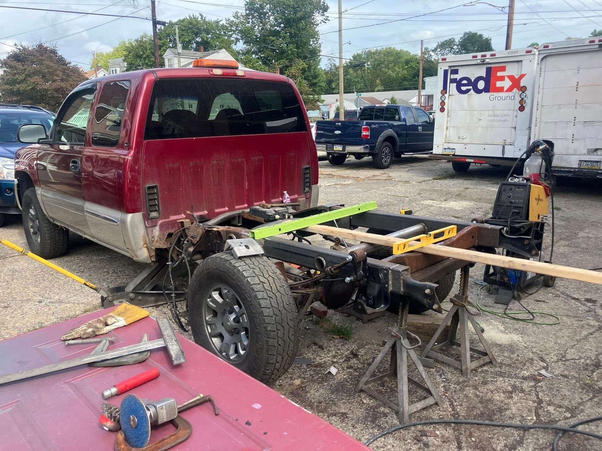 A red truck is being worked on in a parking lot next to a fedex truck.