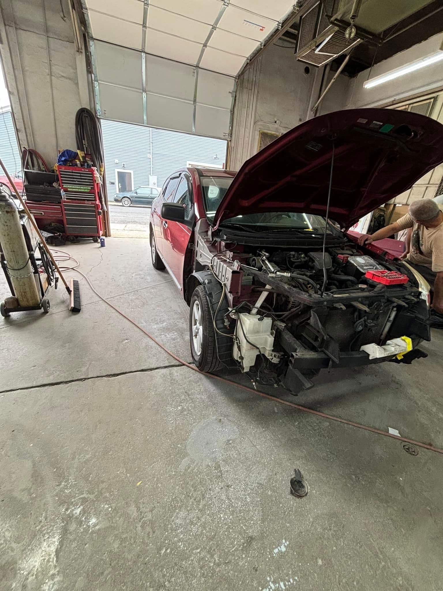 A man is working on a car in a garage with the hood open.