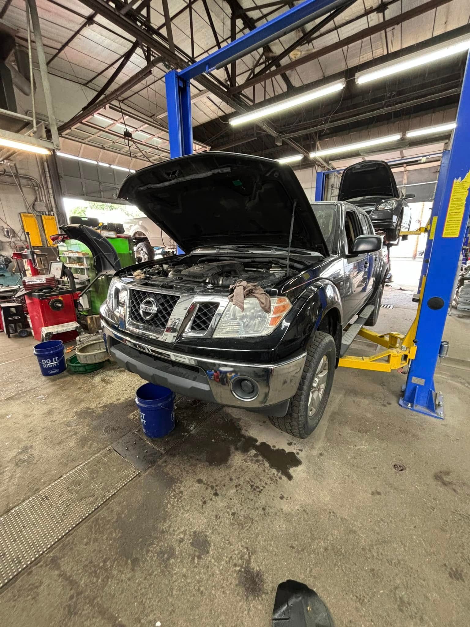 A black truck with the hood up is sitting on a lift in a garage.