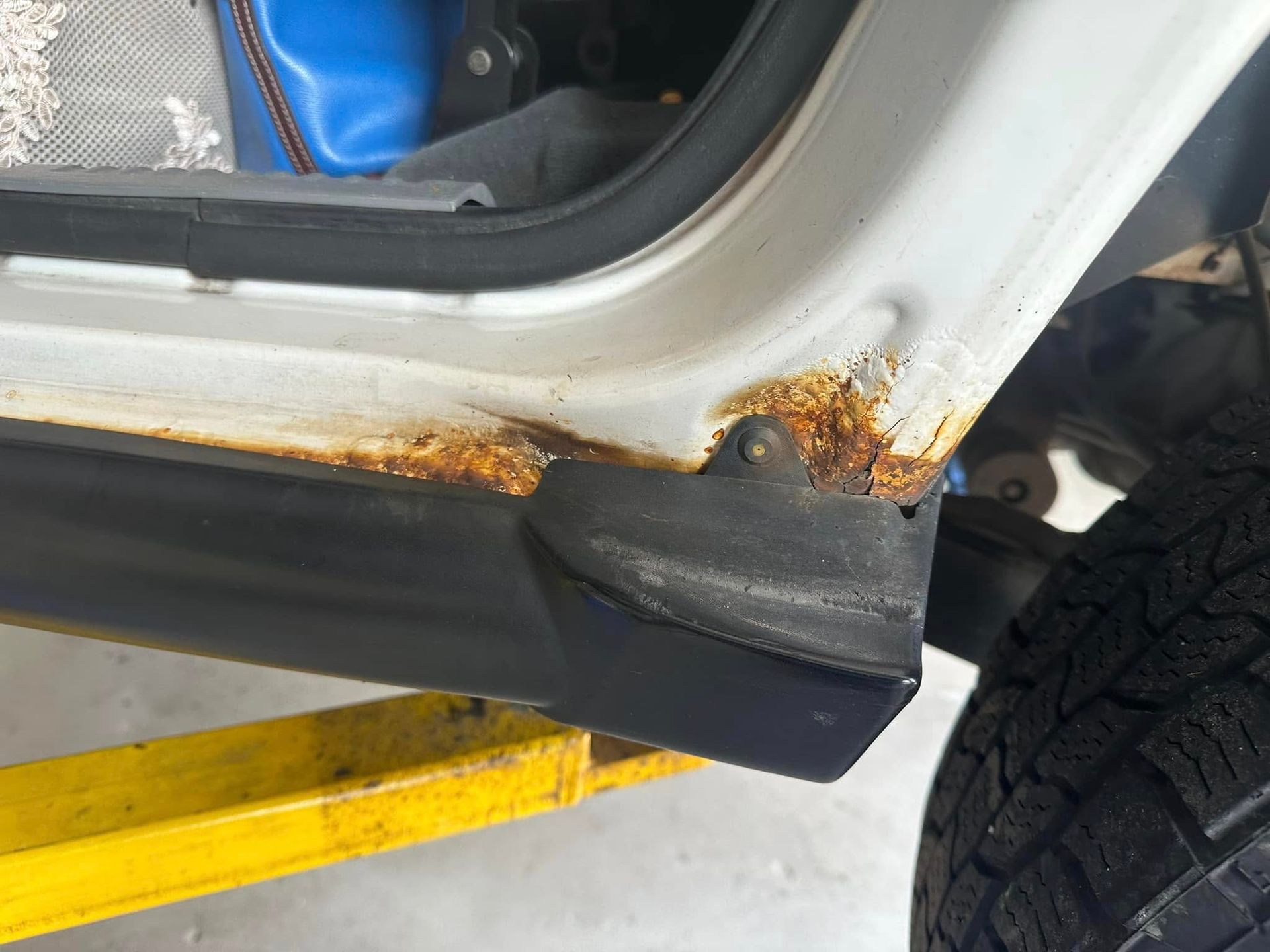 A white car with rust on the side is sitting on a yellow lift.