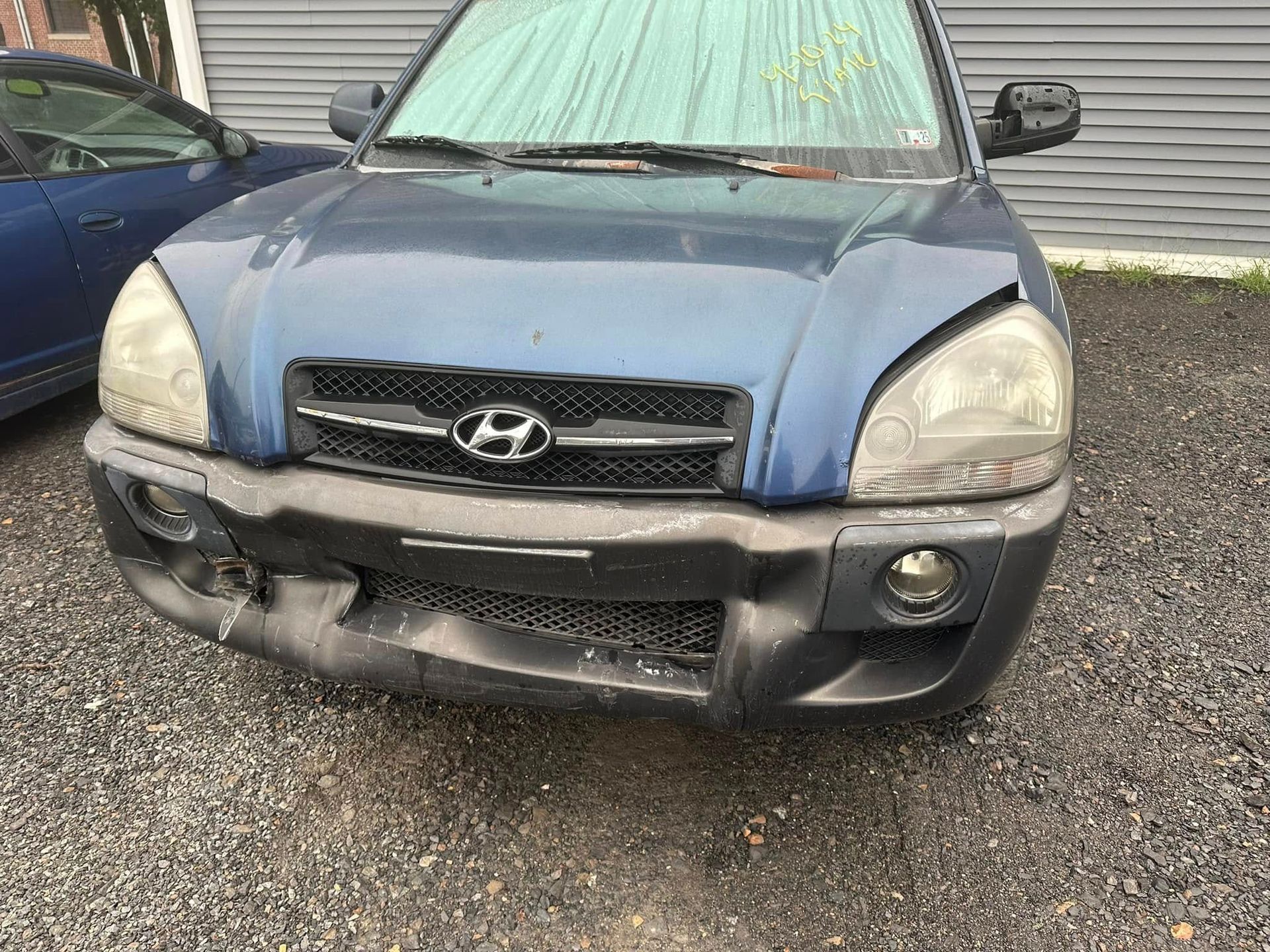 A blue hyundai tucson is parked in a gravel lot.