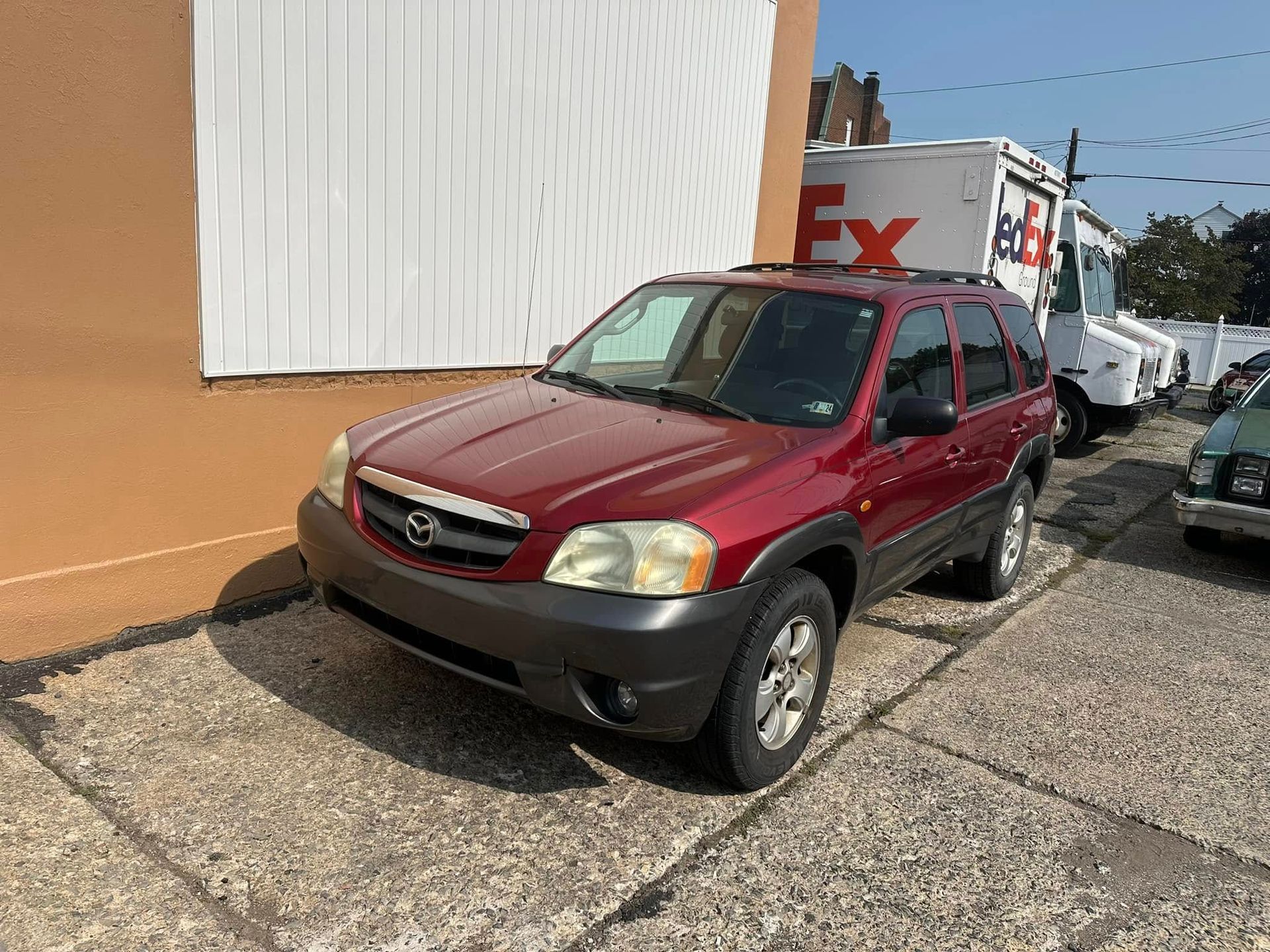A red mazda tribute is parked in front of a fedex truck.