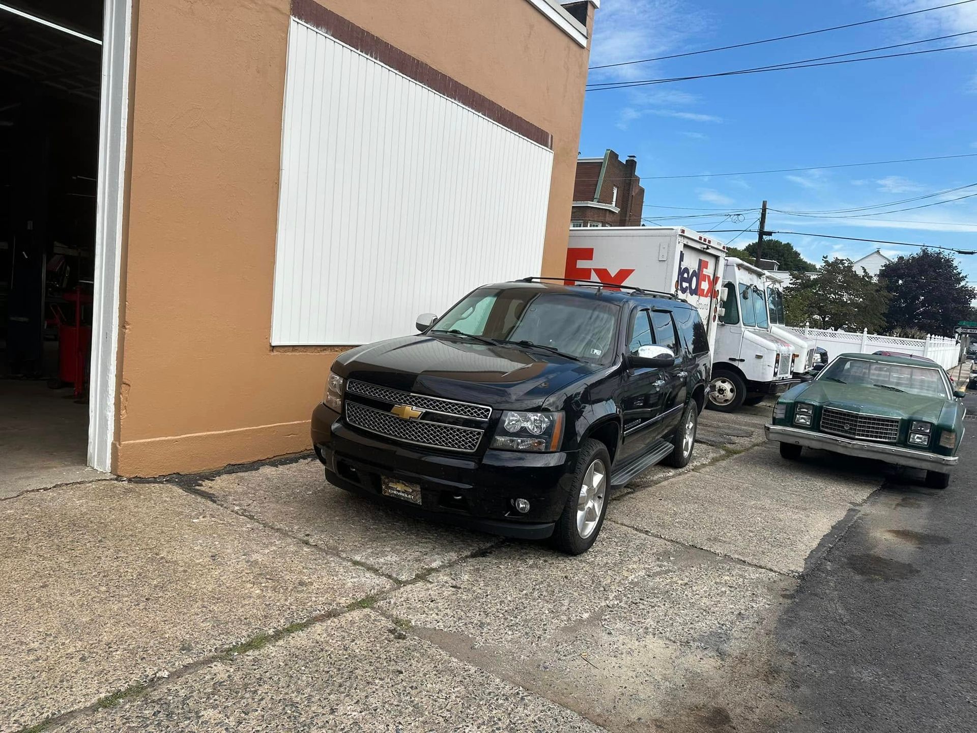 A black suv is parked in front of a building next to a fedex truck.
