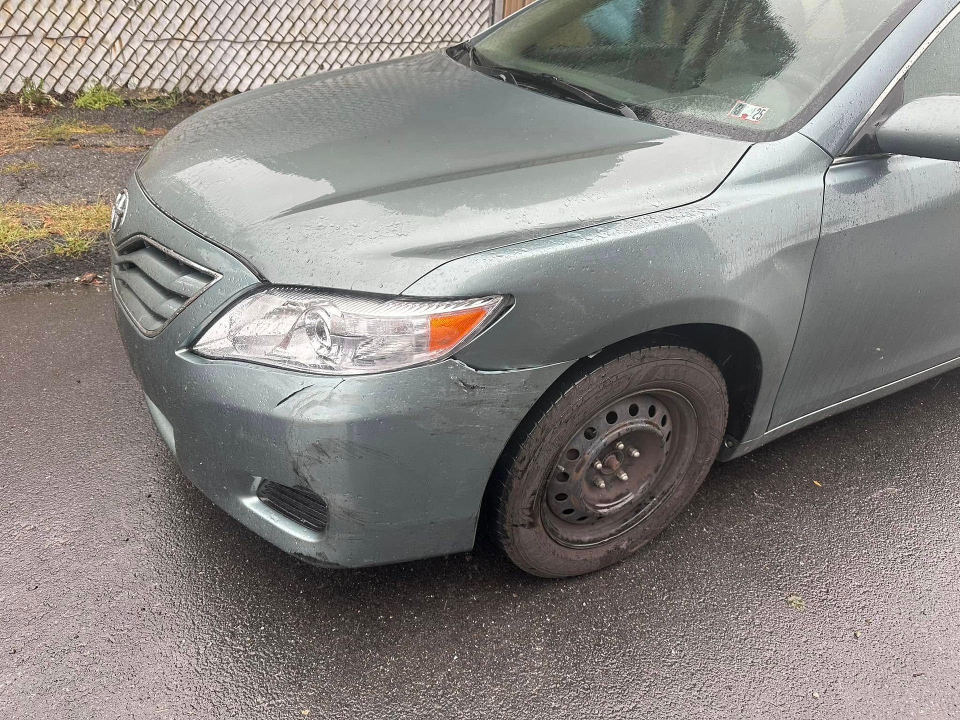 A gray car with a damaged front bumper is parked on the side of the road.