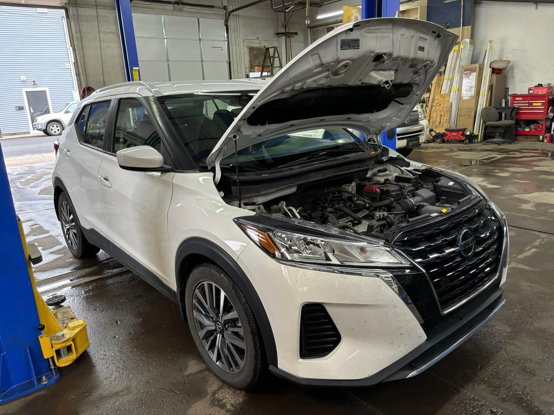 A white nissan kicks with its hood open in a garage.