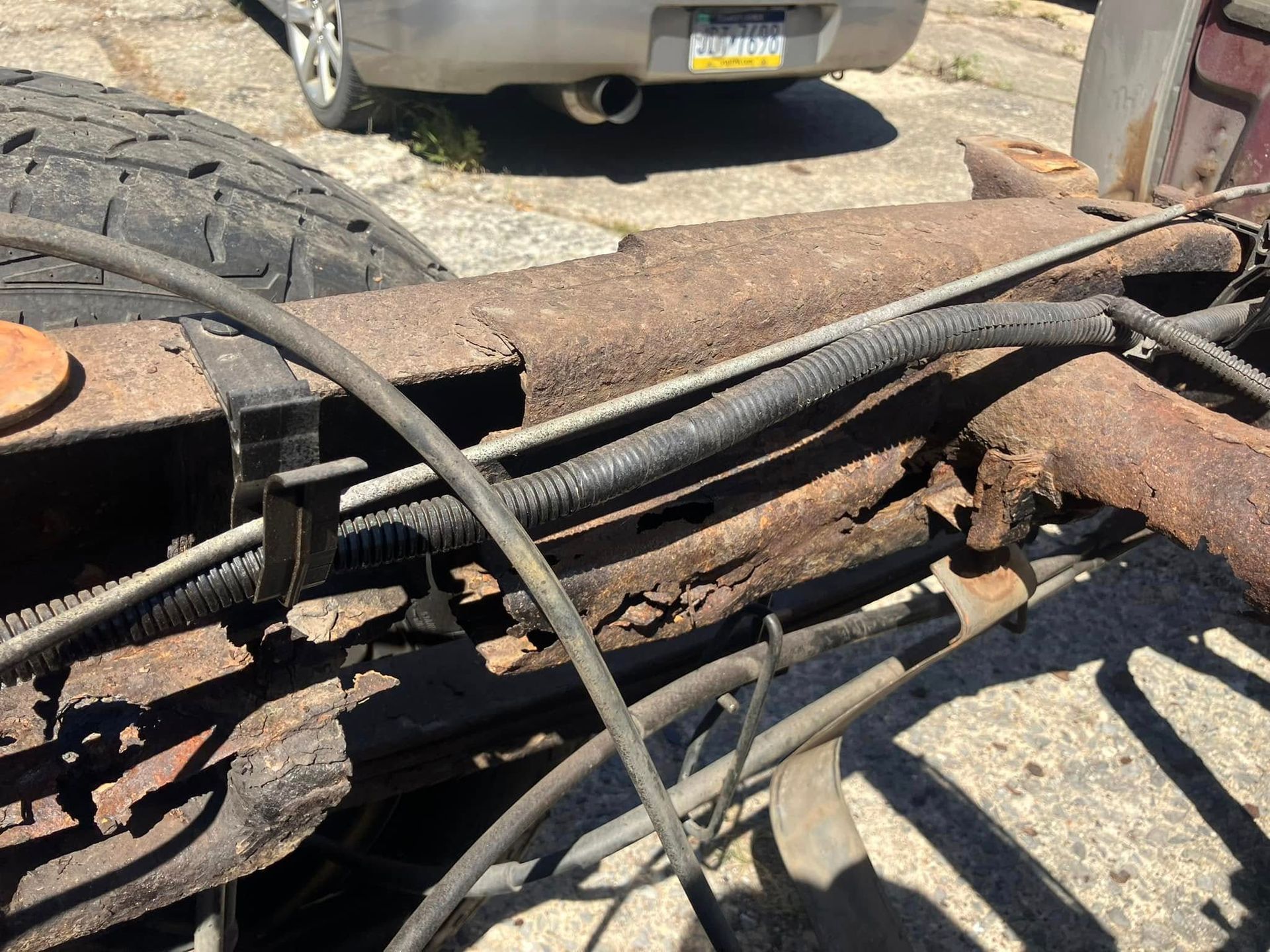 A car is parked in a driveway next to a rusty truck.