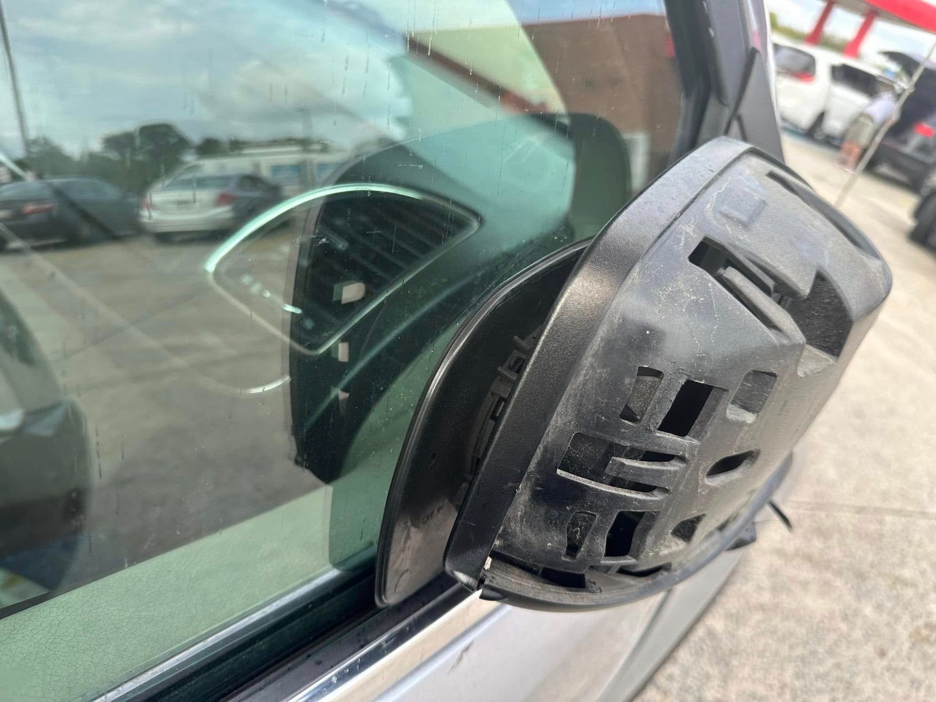 A car with a broken side mirror is parked in a parking lot.