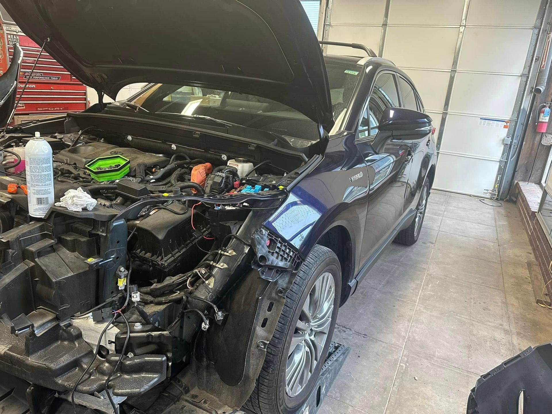 A car is being worked on in a garage with the hood open.