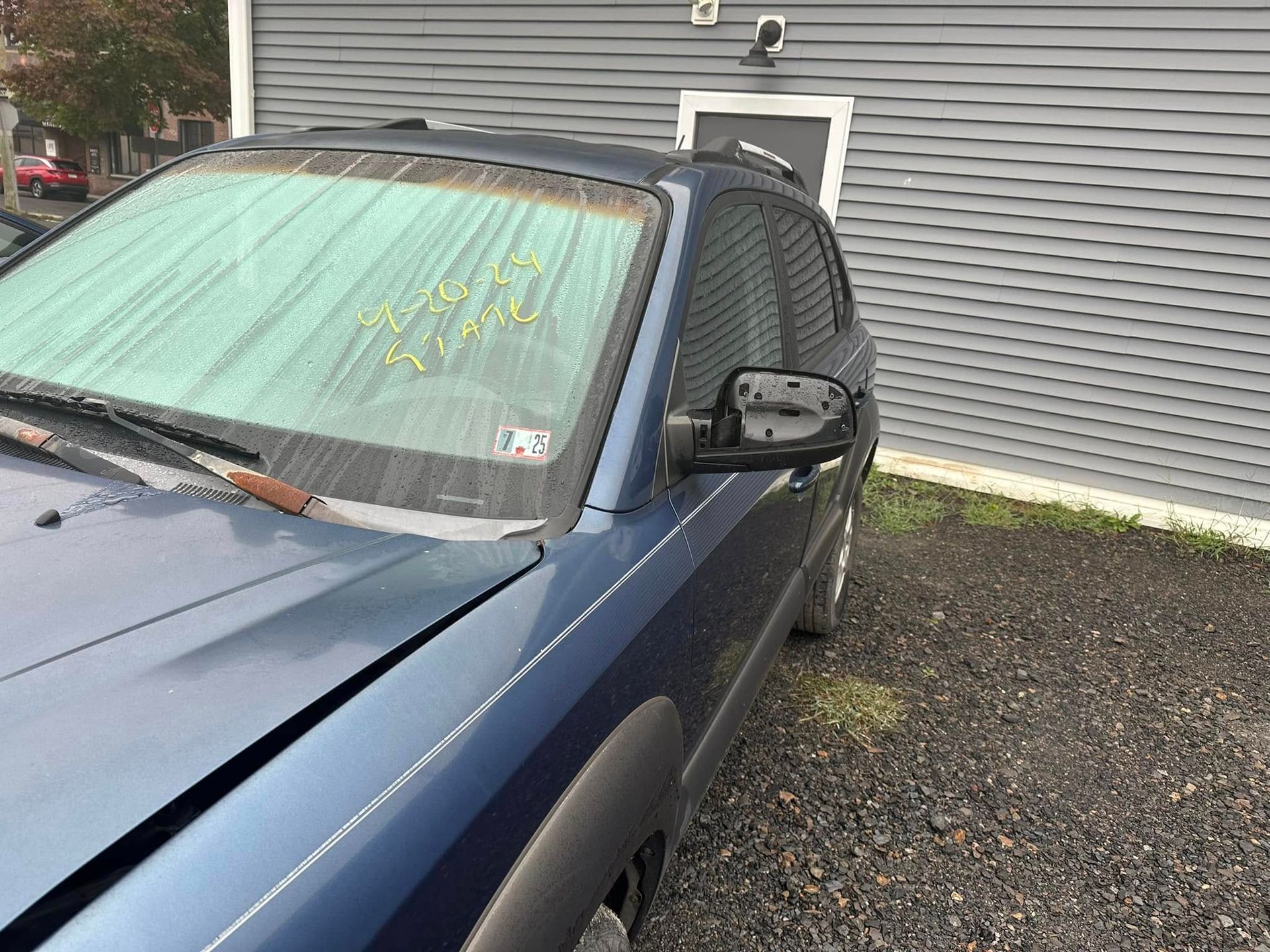 A blue car with a broken windshield is parked in front of a building.