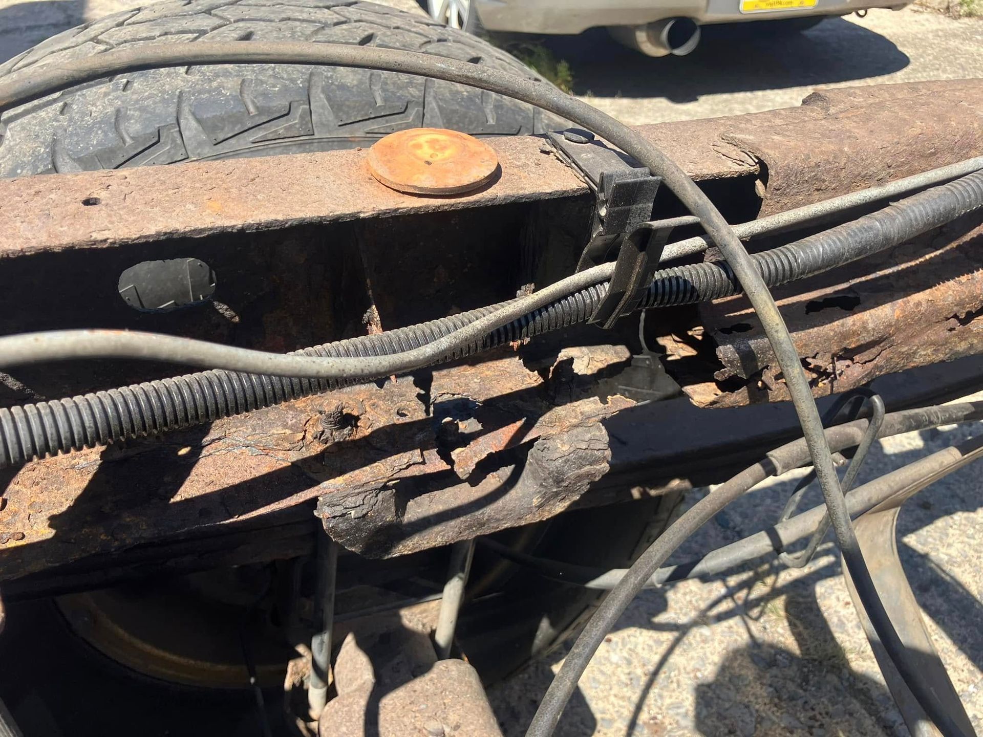 A close up of a rusty vehicle with a car in the background