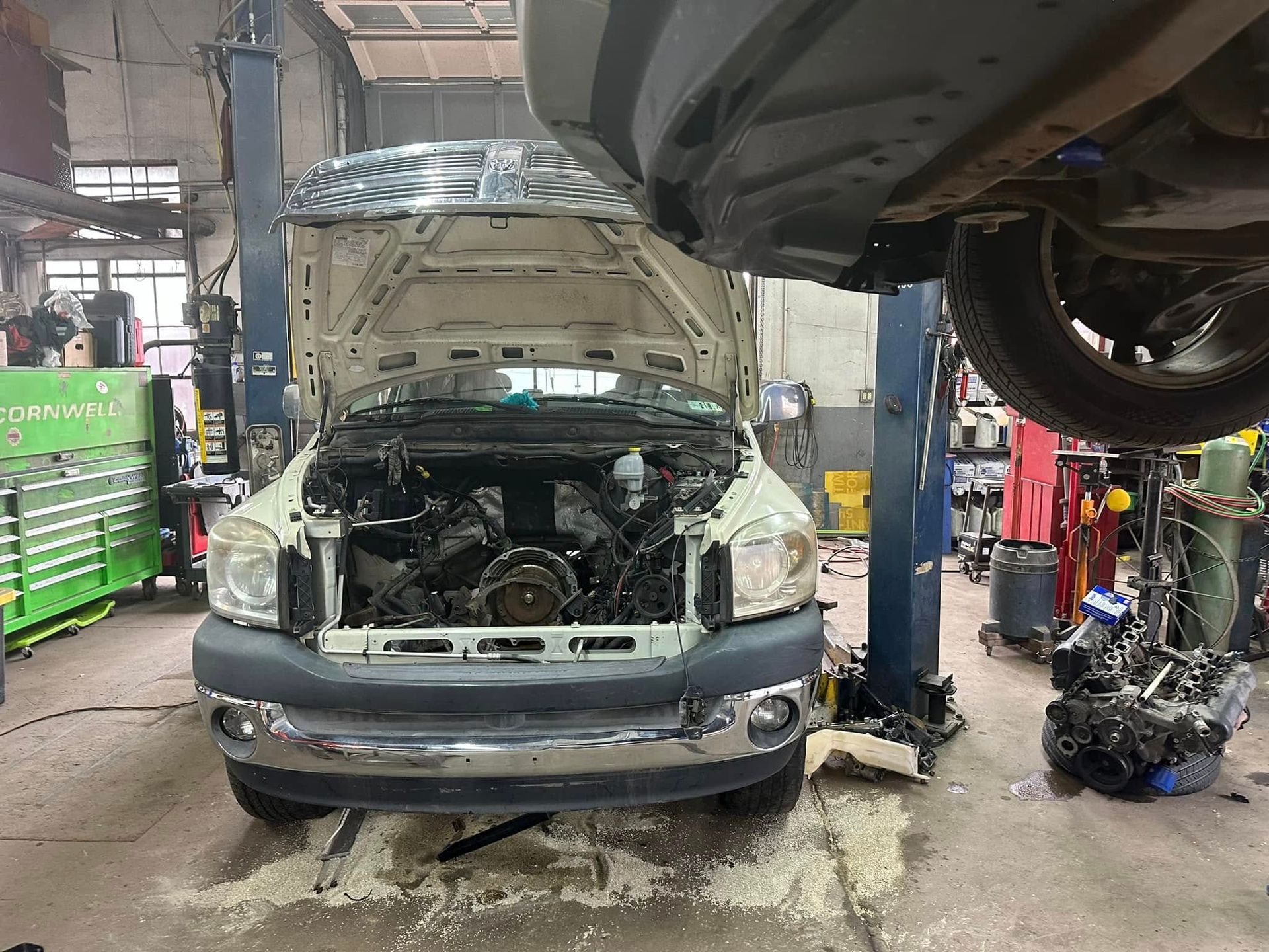 A car with the hood up is sitting on a lift in a garage.