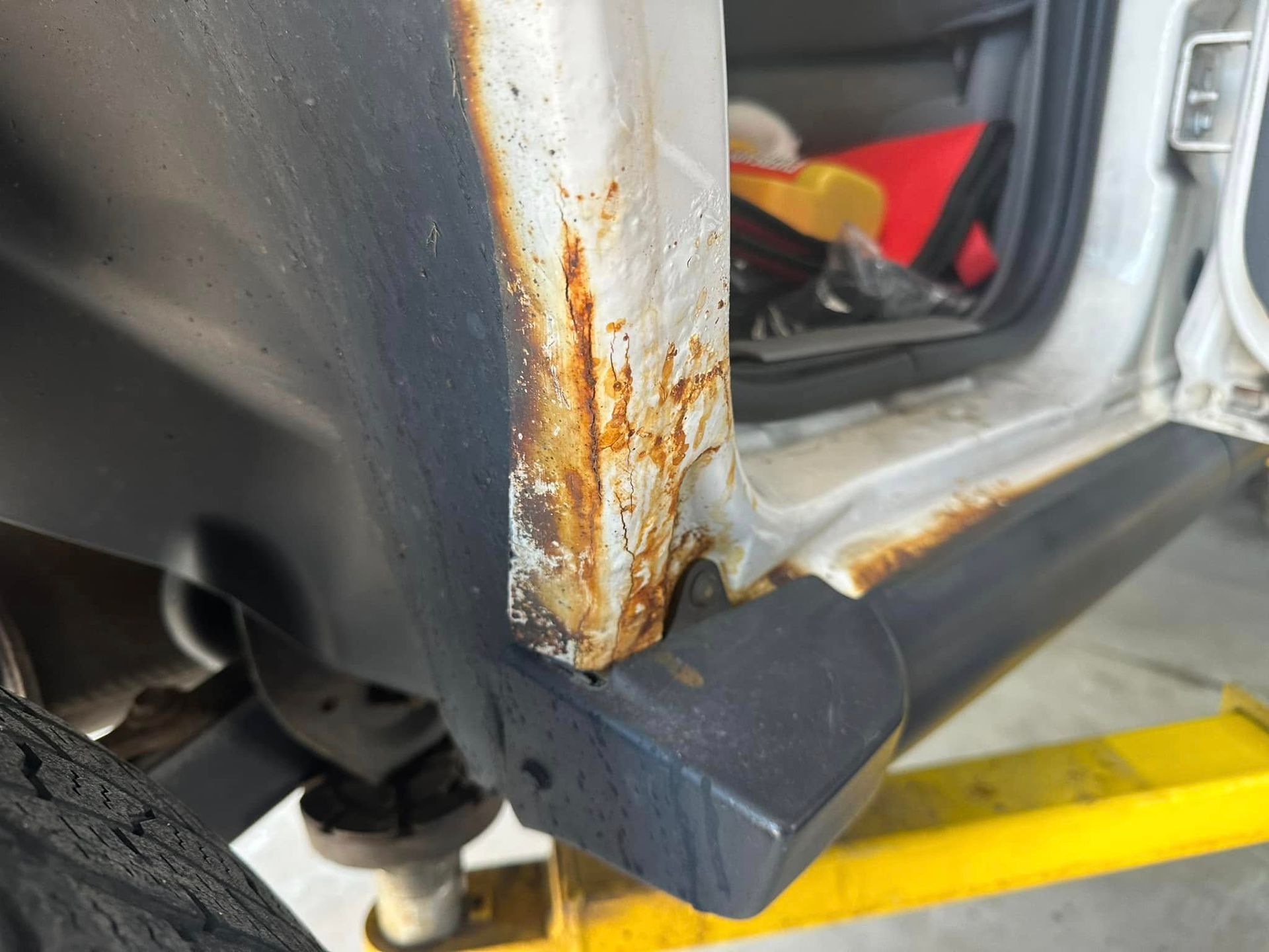 A close up of a rusty fender on a white car.