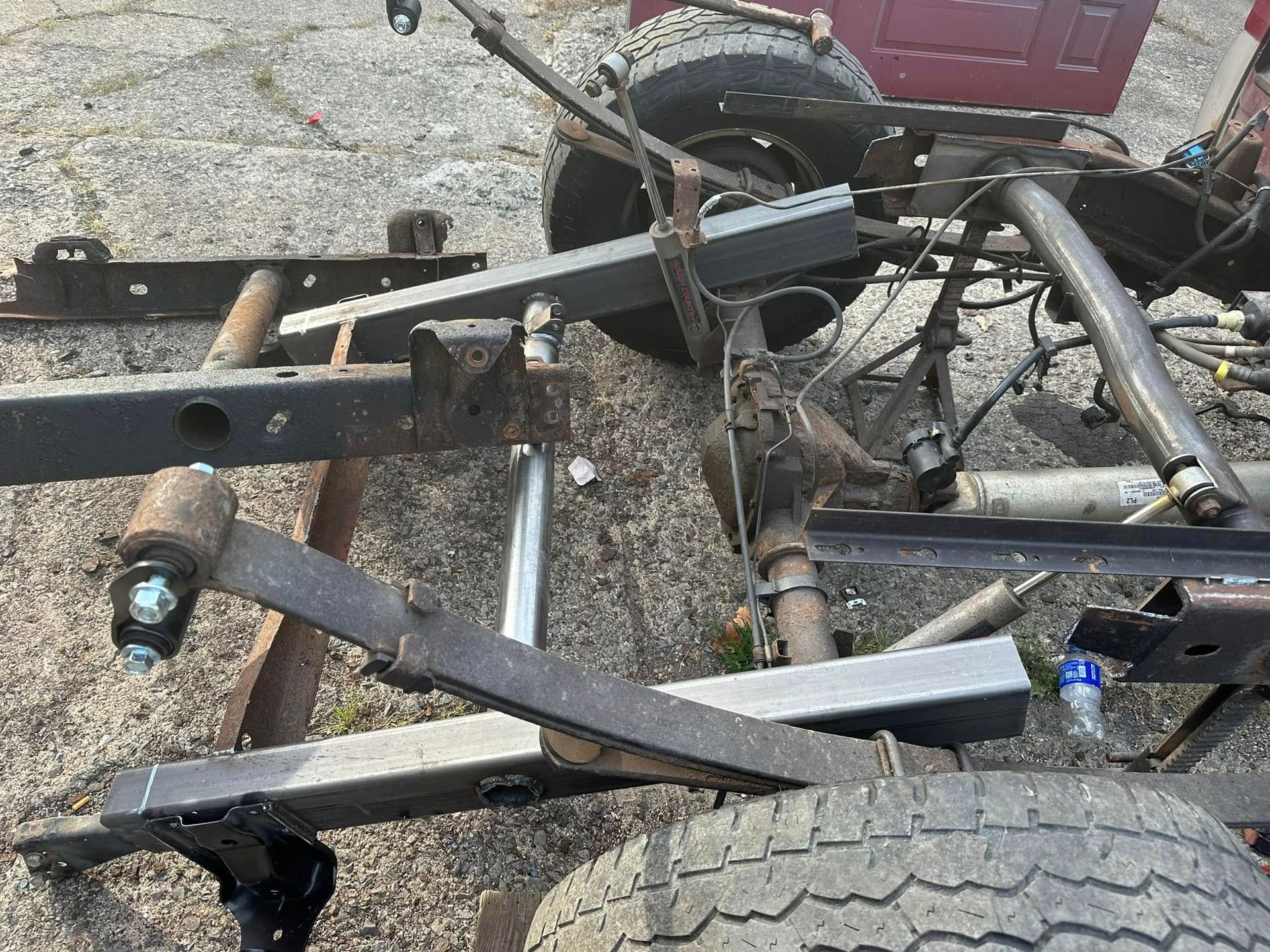 A truck frame is sitting on the ground next to a tire.