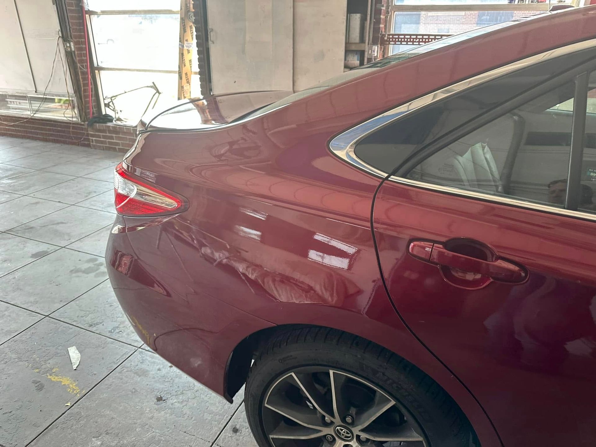 A red car is parked in a garage next to a window.