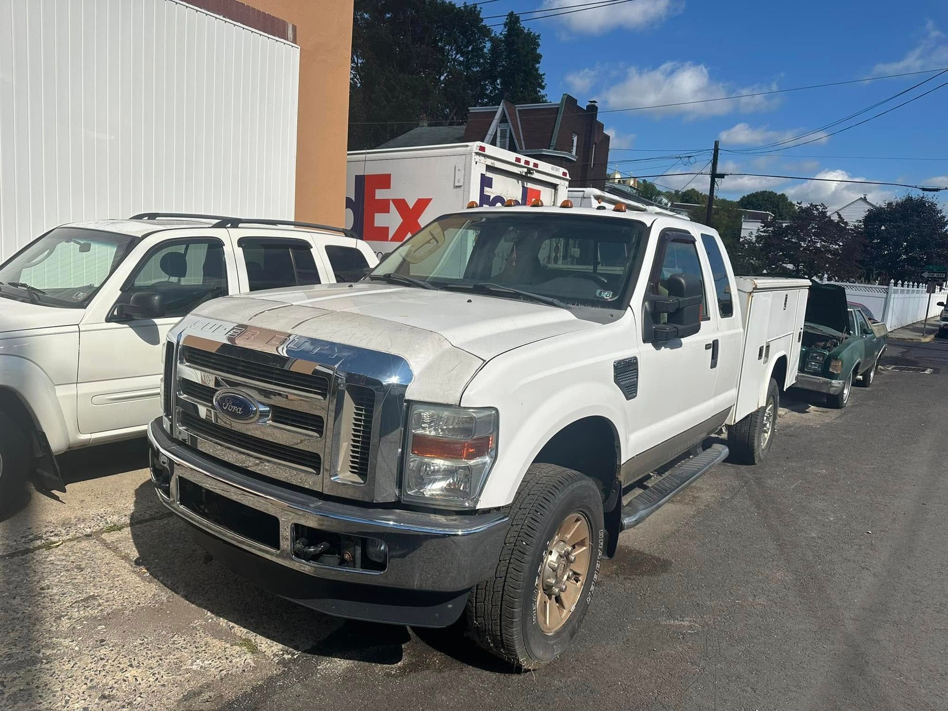 A white truck is parked in front of a fedex truck.
