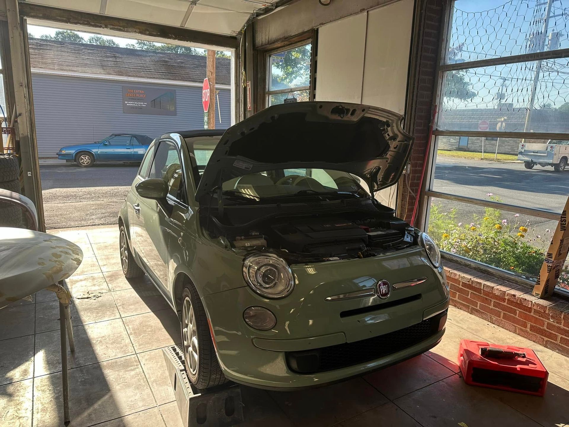 A green car with the hood up is sitting in a garage.