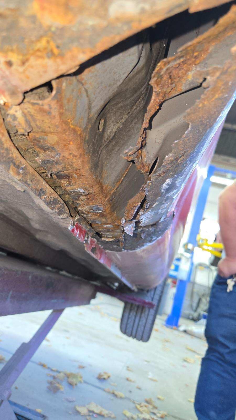 A man is standing next to a rusty car in a garage.