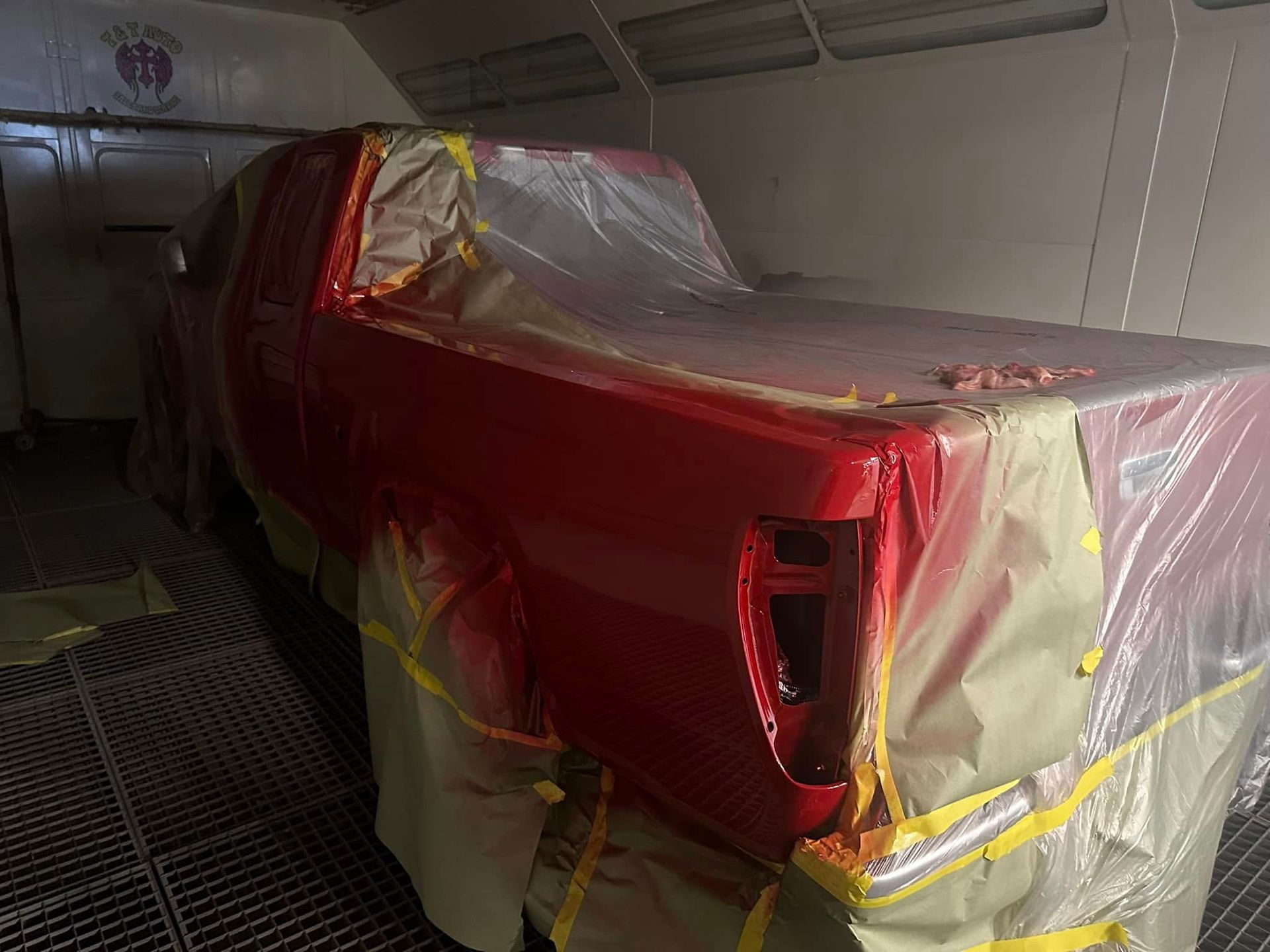 A red truck is being painted in a paint booth.