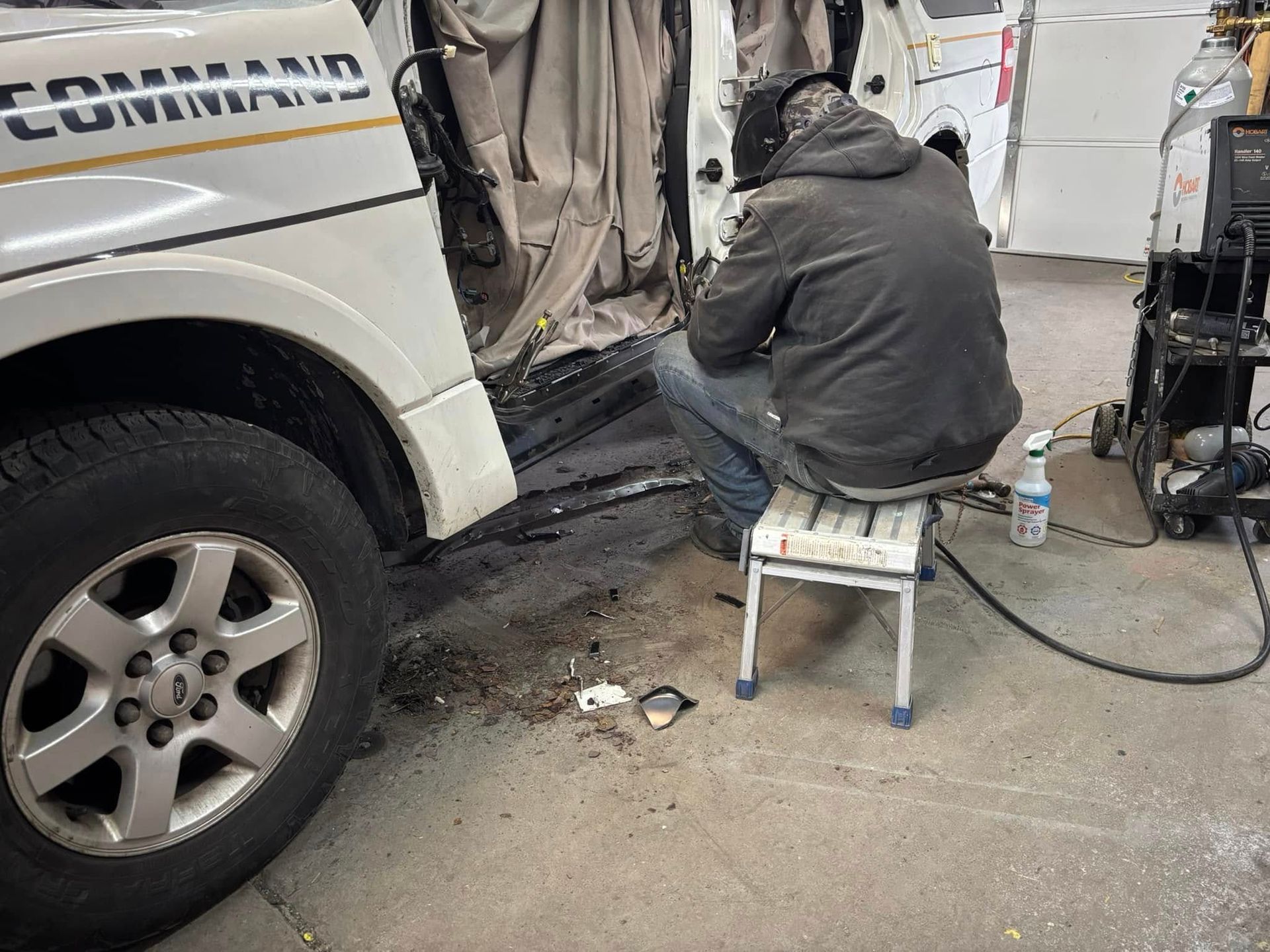 A man is sitting on a stool in front of a white truck.