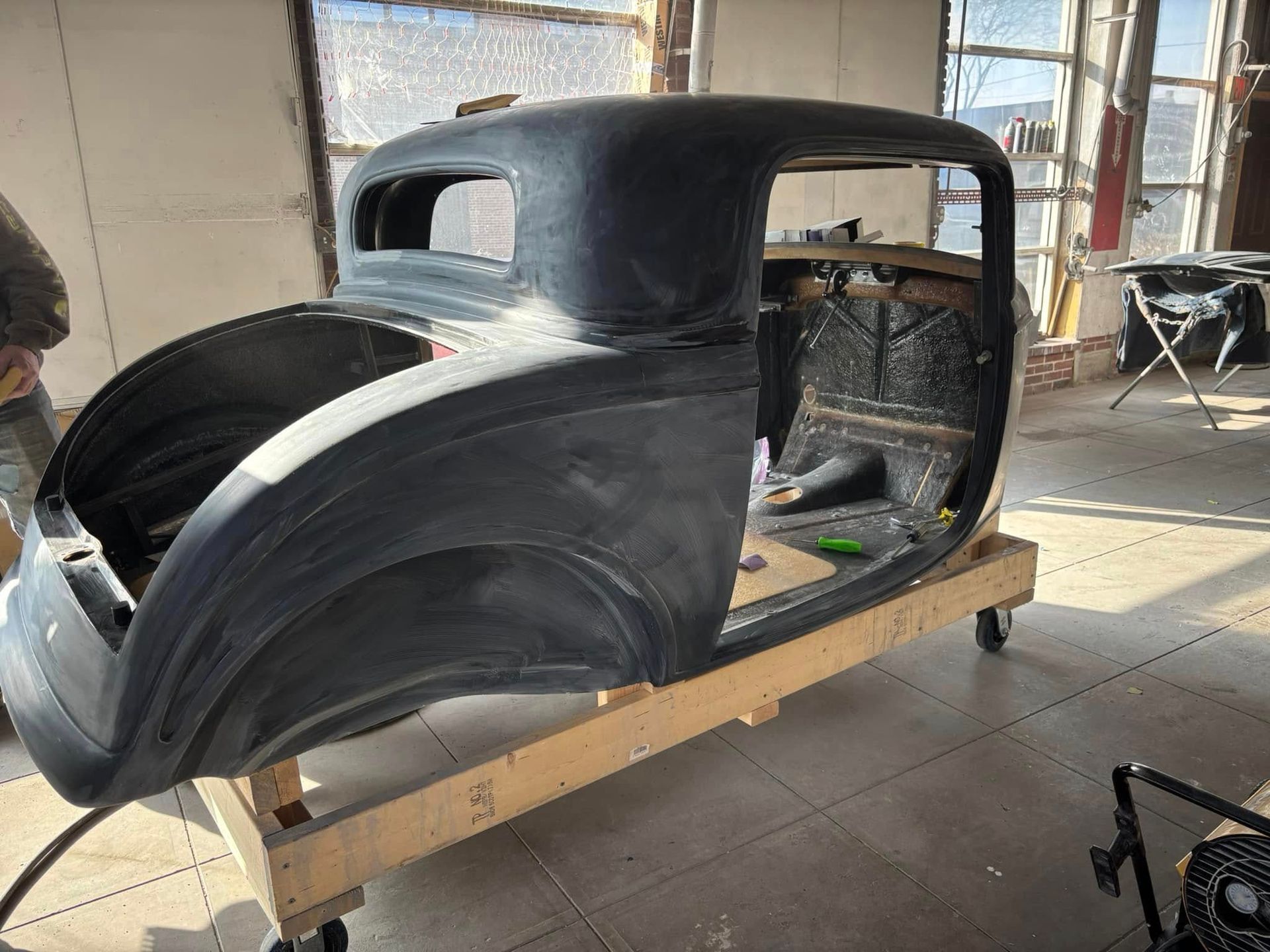 A black car is sitting on a wooden pallet in a garage.