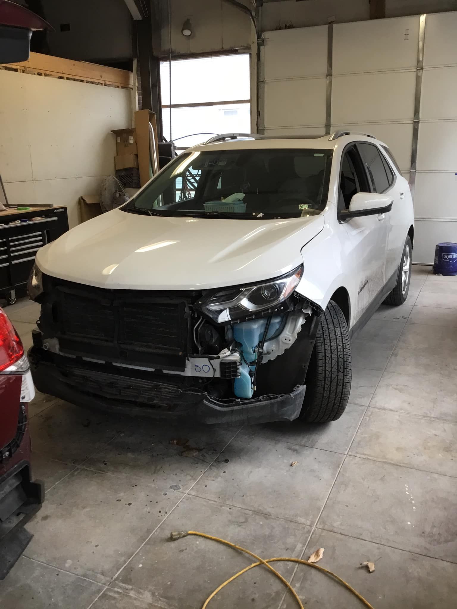 A white suv with a damaged front end is parked in a garage.