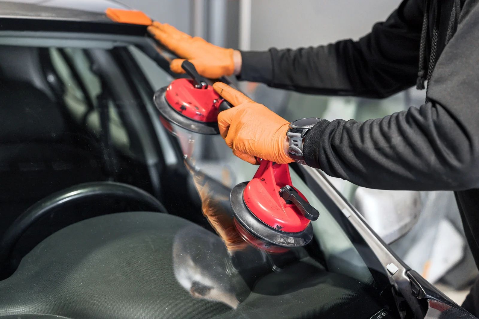 Person in orange gloves uses suction cups to remove a windshield from a car.