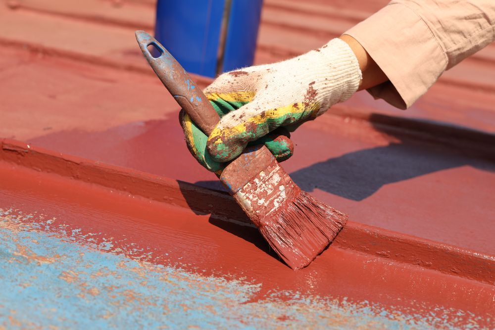 Person Painting a Metal Roof Red With a Paintbrush — Israel Jones Painting in Idalia, QLD