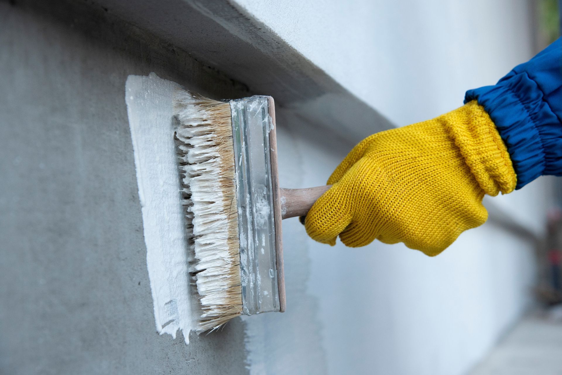 Hand in Yellow Glove Using Brush to Apply Sealant to a Wall — Israel Jones Painting in Rowes Bay, QLD