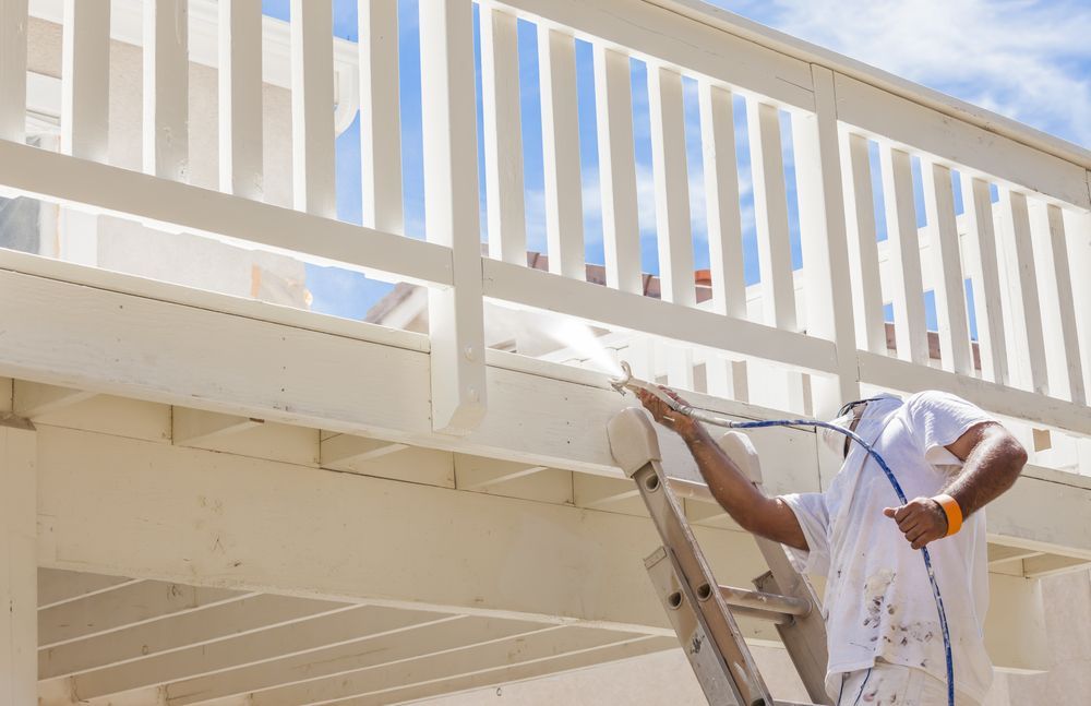 Person on a Ladder Painting a White Railing With a Spray Gun — Israel Jones Painting in Pallarenda, QLD