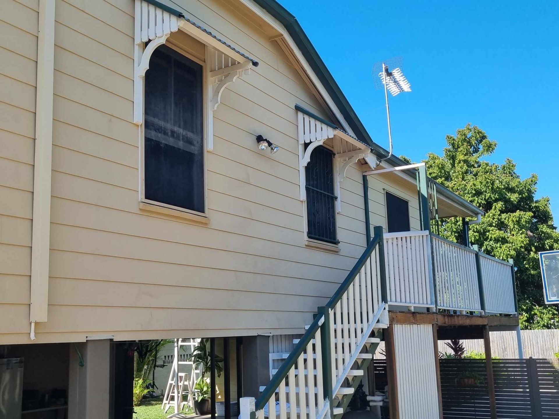A two-story house with cream siding, white trim, and a porch, set against a blue sky — Israel Jones Painting in Vincent, QLD