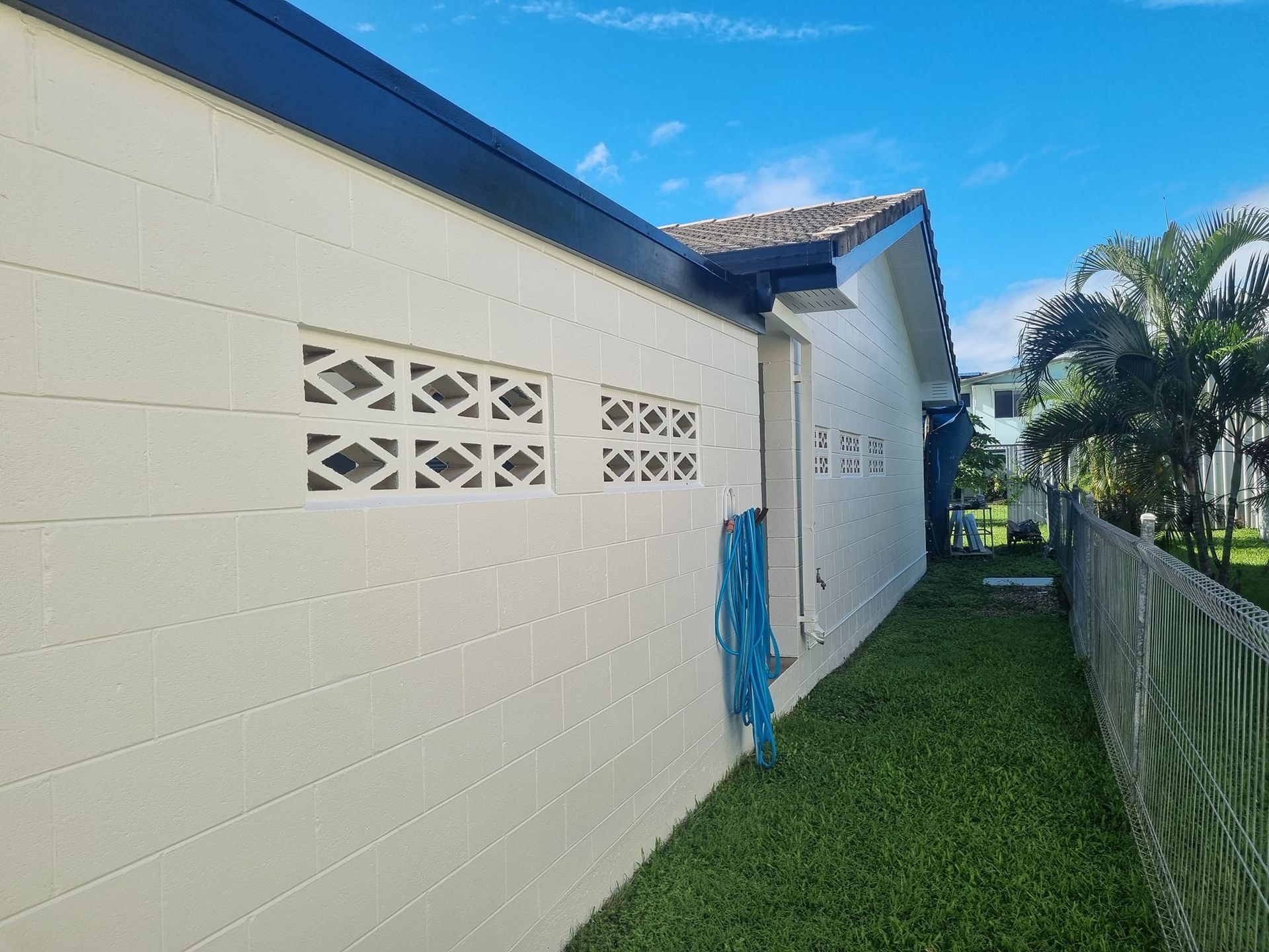 Cream-colored concrete block building with decorative vents, blue hose, and green lawn under a blue sky — Israel Jones Painting in Vincent, QLD