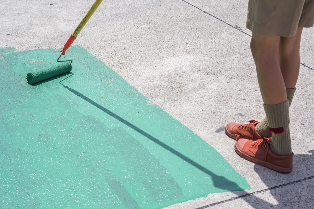 Person Painting a Concrete Surface Green With a Roller — Israel Jones Painting in Vincent, QLD