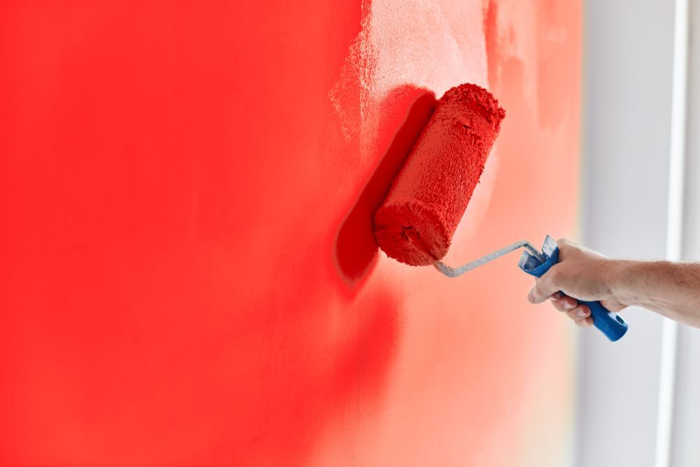 Person Painting a Wall With a Red Paint Roller — Israel Jones Painting in Idalia, QLD