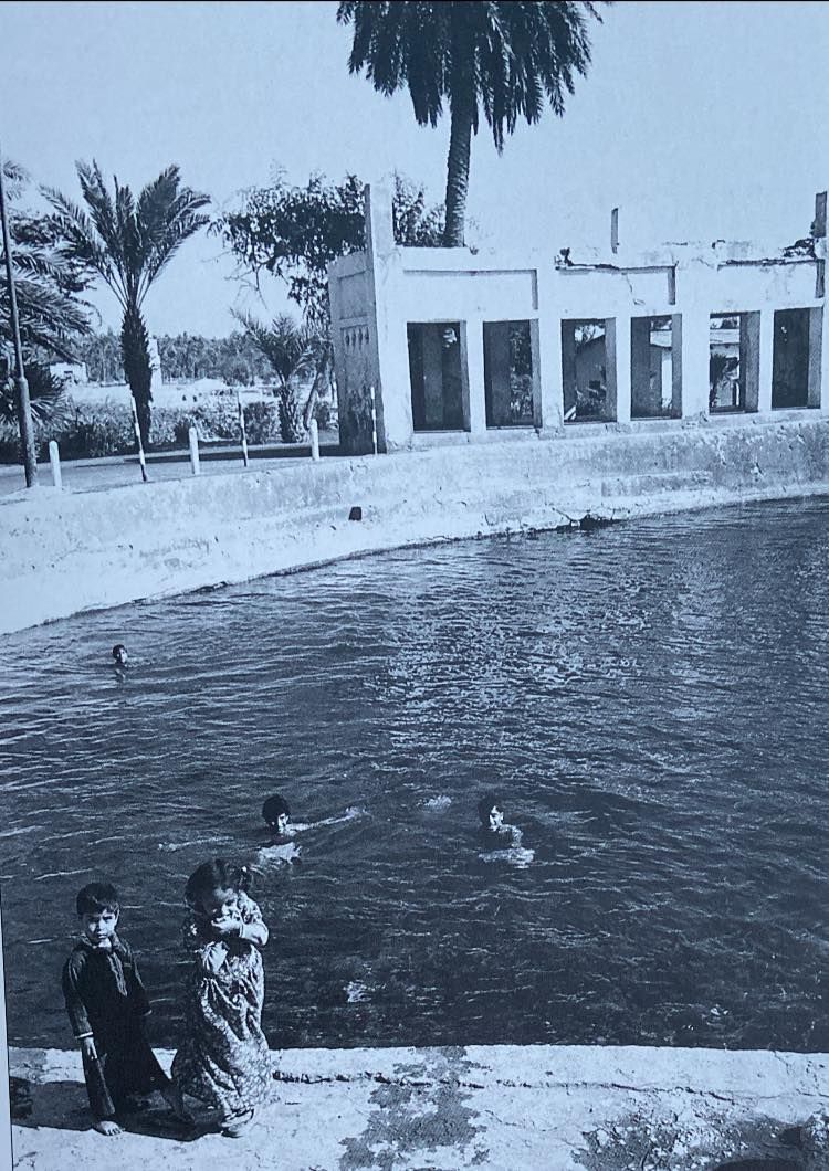 Ain Adhari BW with the old building now crumbling. We see roadways leading up to it and the date palms have receeded into the background