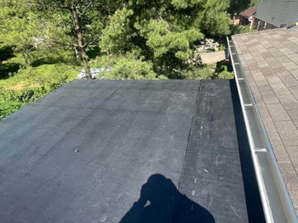A person is taking a picture of a roof with trees in the background.