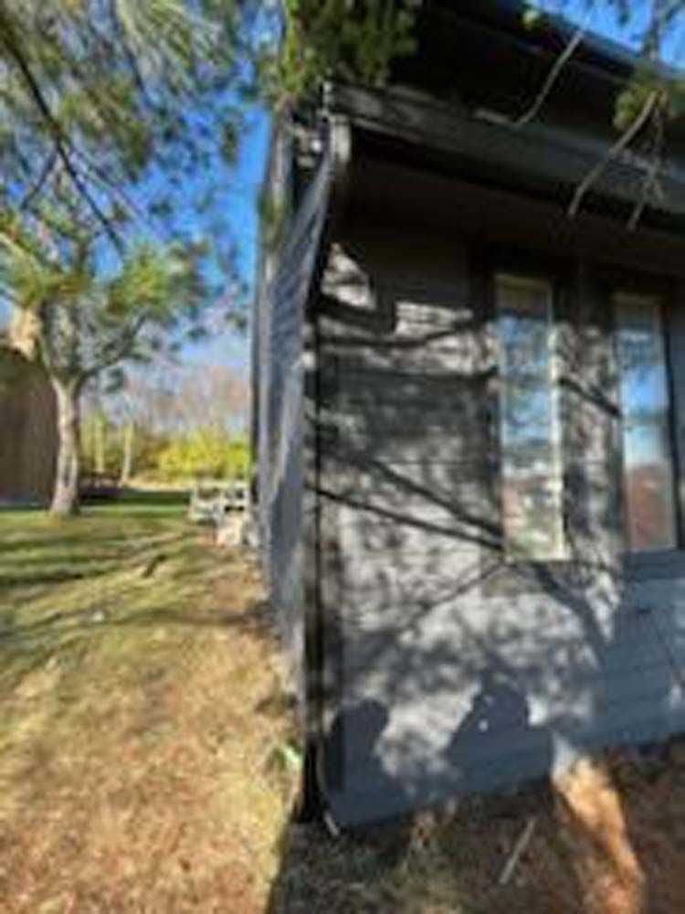A small house is sitting in the middle of a field next to a tree.