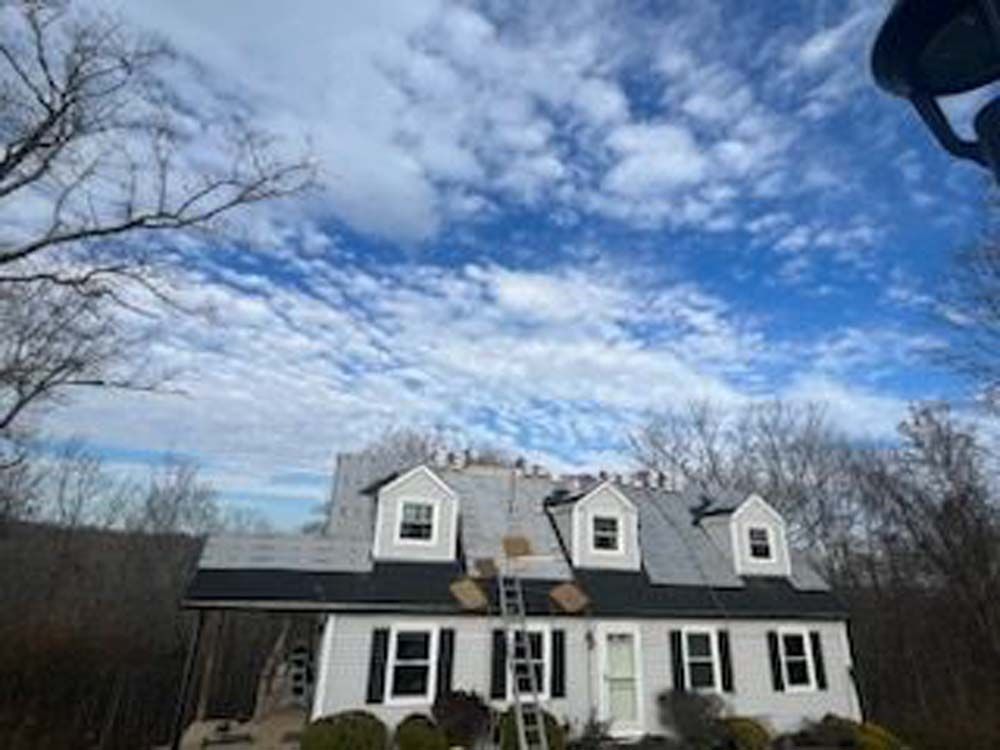 A large white house with a black roof is being remodeled.